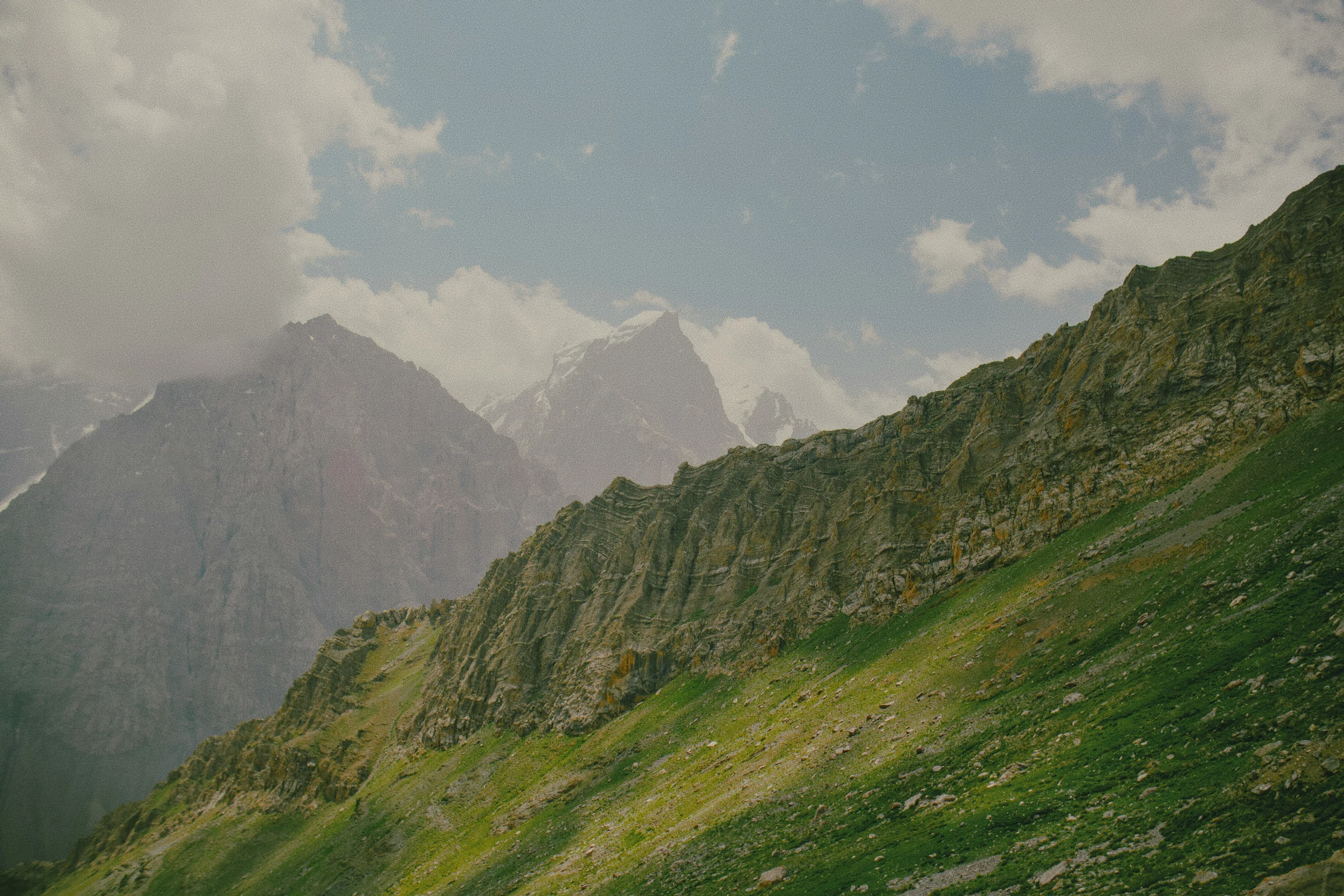 Green alpine slopes beneath rugged mountains and soft clouds